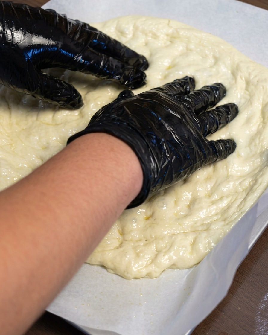 Des mains étirant la pâte à pizza vers lextérieur sur une feuille de papier sulfurisé.