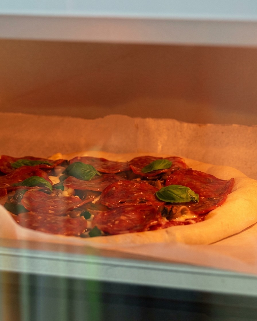 Une pizza crue garnie de fromage, de champignons et de pepperoni délicatement enfournée dans un four chaud.
