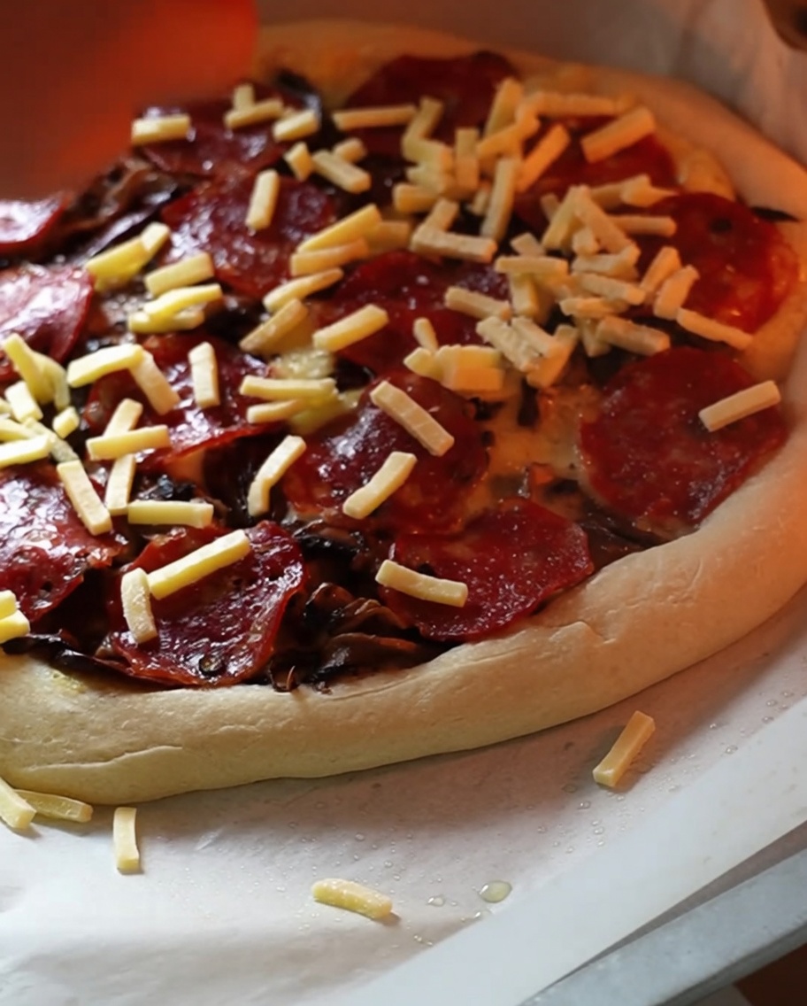 Une pizza partiellement cuite dans un four recevant une généreuse pincée finale de fromage râpé.