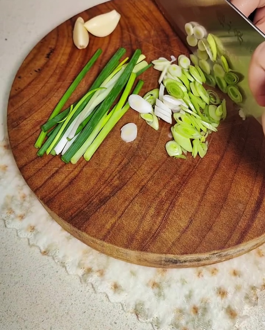 Oignons verts et gousses dail en cours de découpe sur une planche en bois.