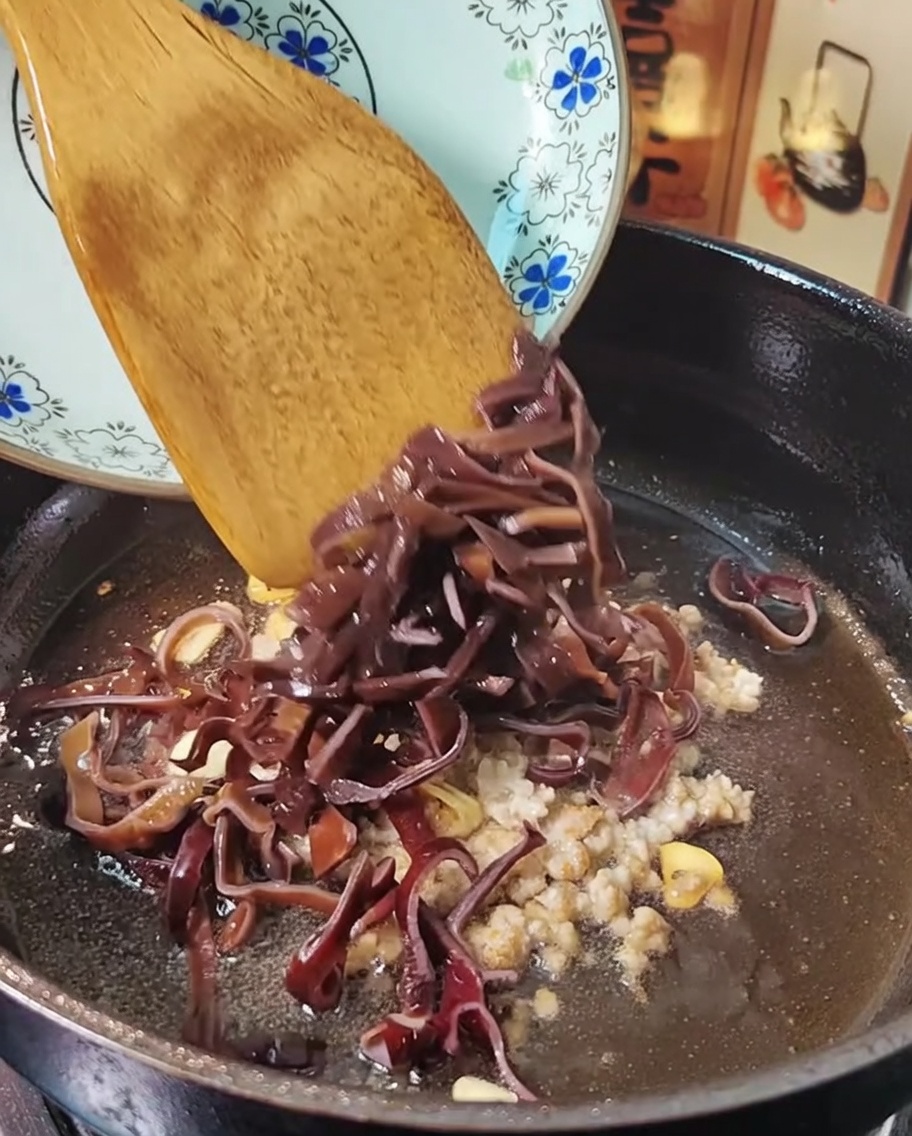 Viande hachée et champignons noirs sautant dans une poêle avec une spatule en bois.