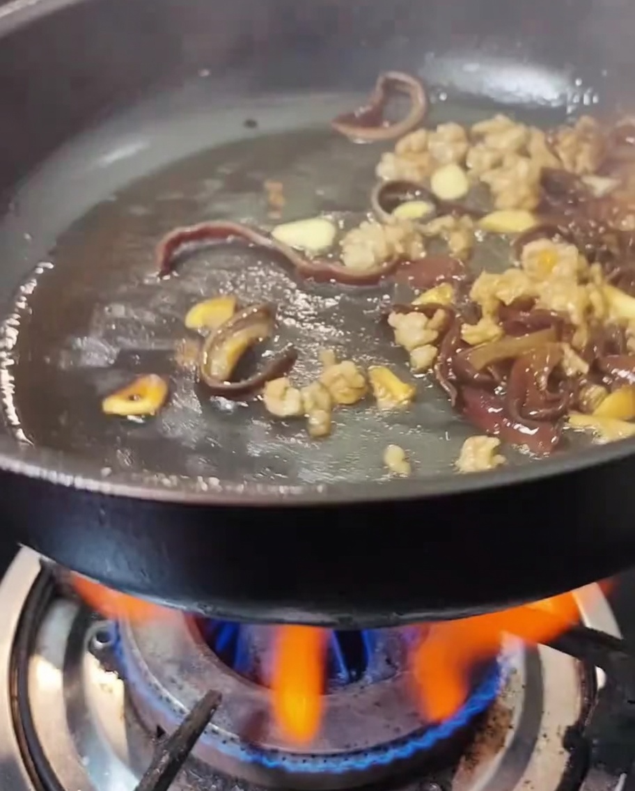 Sauce soja claire et sauce huître versées dans une poêle contenant la viande et les champignons.