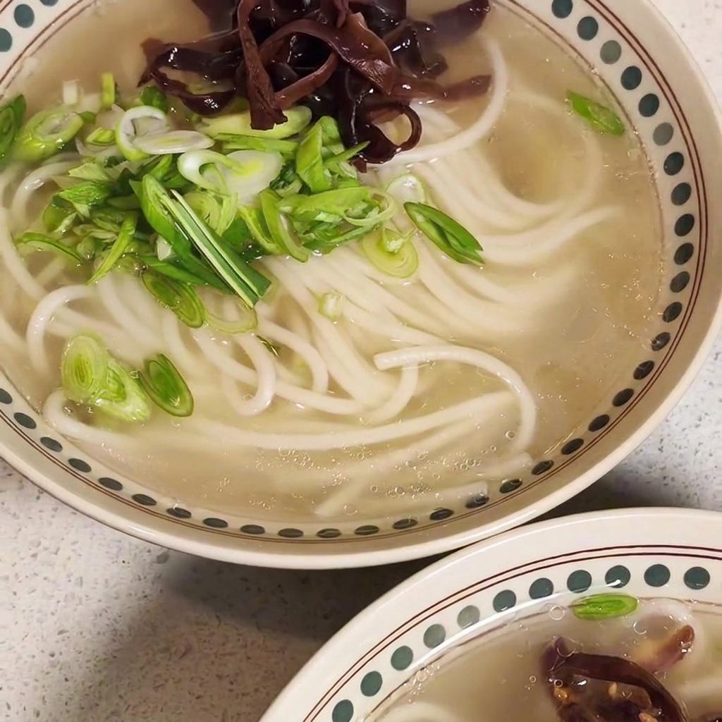 Un bol de ramen presque terminé surmonté de viande sautée, de champignons et doignons verts.
