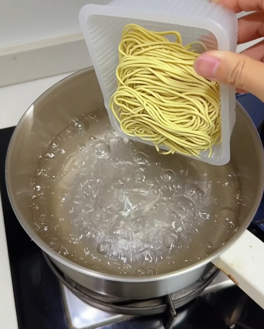 Un bloc de nouilles ramen fraîches plongé dans une casserole deau bouillante.