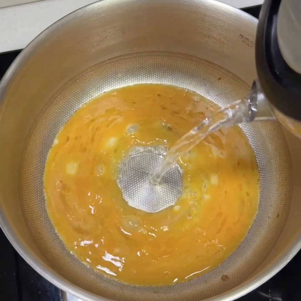 De leau bouillante est versée sur la base tonkotsu, formant un bouillon blanc et crémeux.