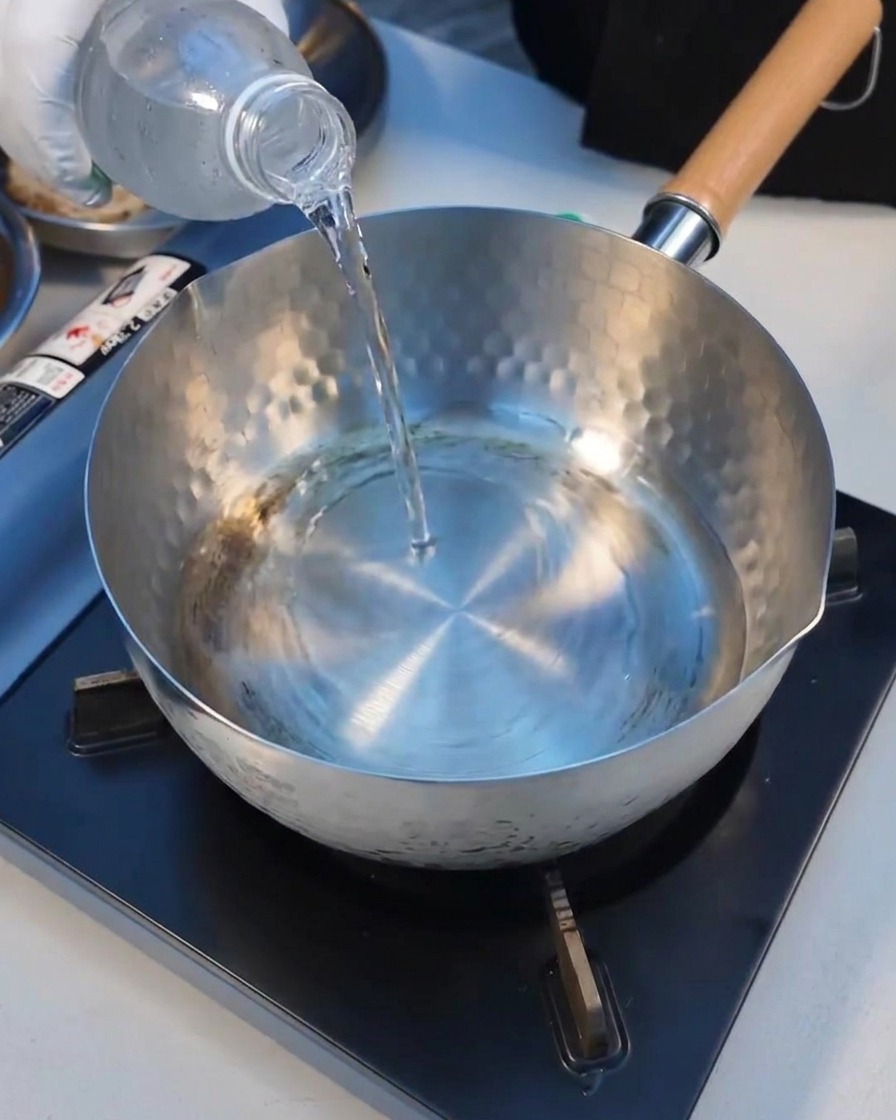Versement de leau minérale dans une casserole en métal sur la plaque de cuisson.