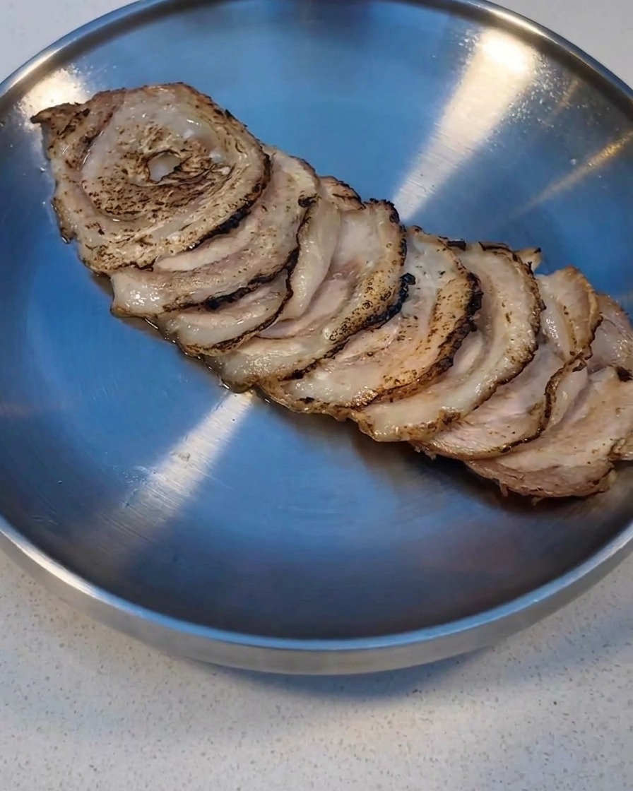 Tranches de Char Siu grillées à laide dun chalumeau de cuisine sur une plaque métallique.