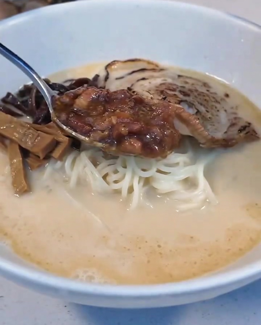 Une cuillère de sauce à la viande braisée et un demi œuf mollet déposés sur les nouilles.