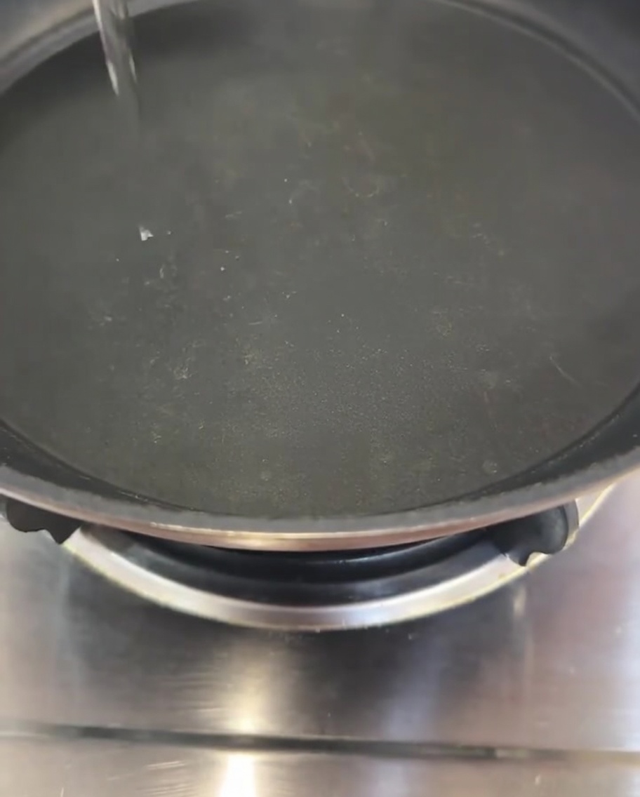 Un filet mince et clair dhuile de cuisson versé au centre dune poêle à frire noire.
