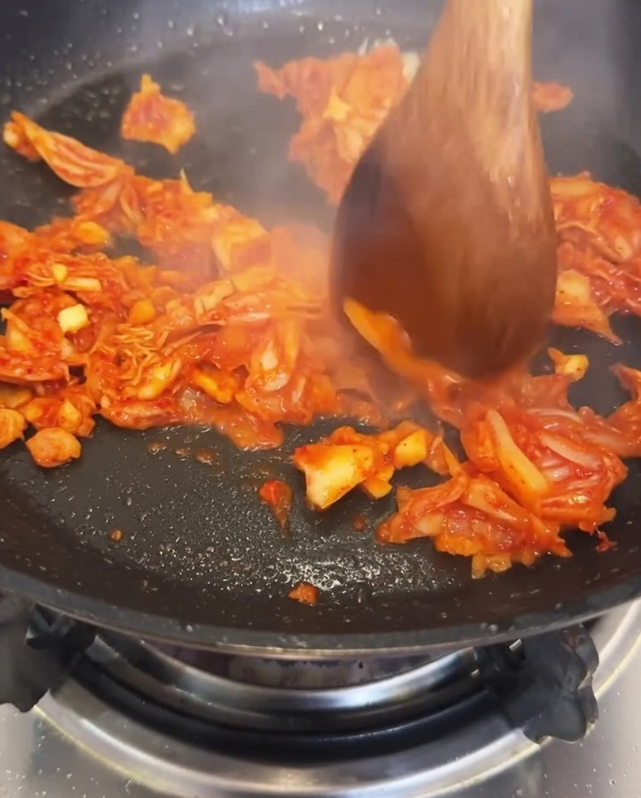 De leau versée dans la poêle contenant le kimchi et lail sautés.