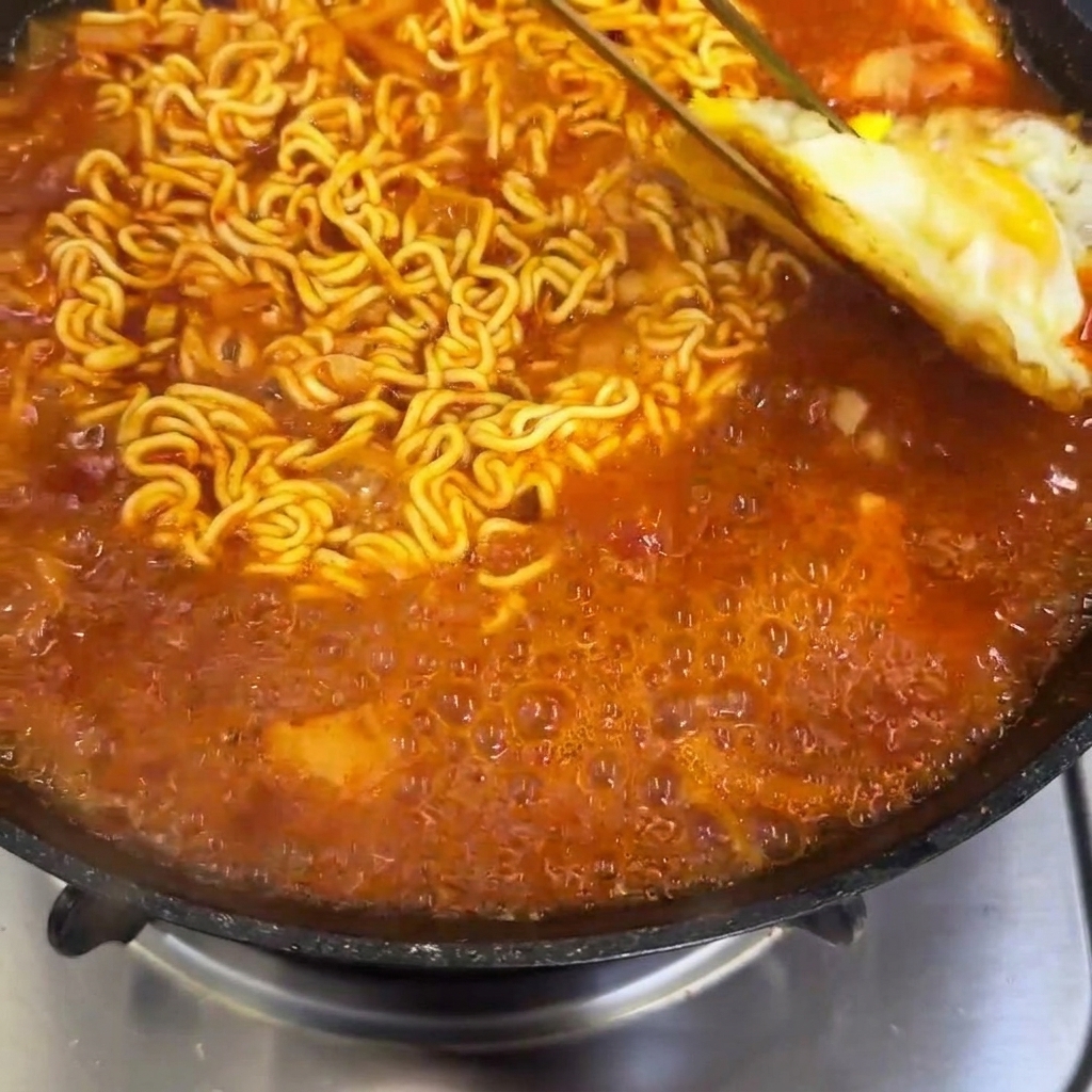 Des œufs frits placés dans une poêle avec des nouilles ramen épicées mijotantes.