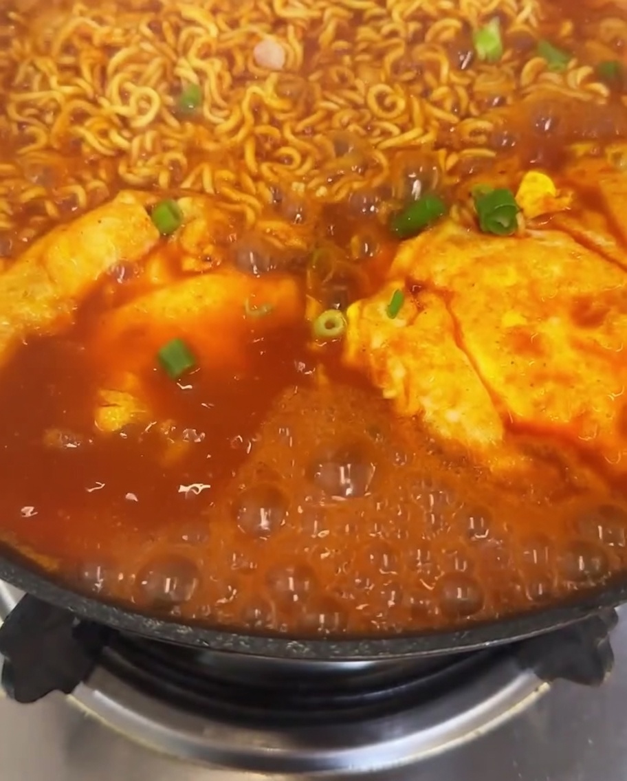 Une vue rapprochée dune casserole de ramen au kimchi garnie doignons verts fraîchement parsemés et de tranches de piment rouge vif, avec le bouillon bouillonnant autour.