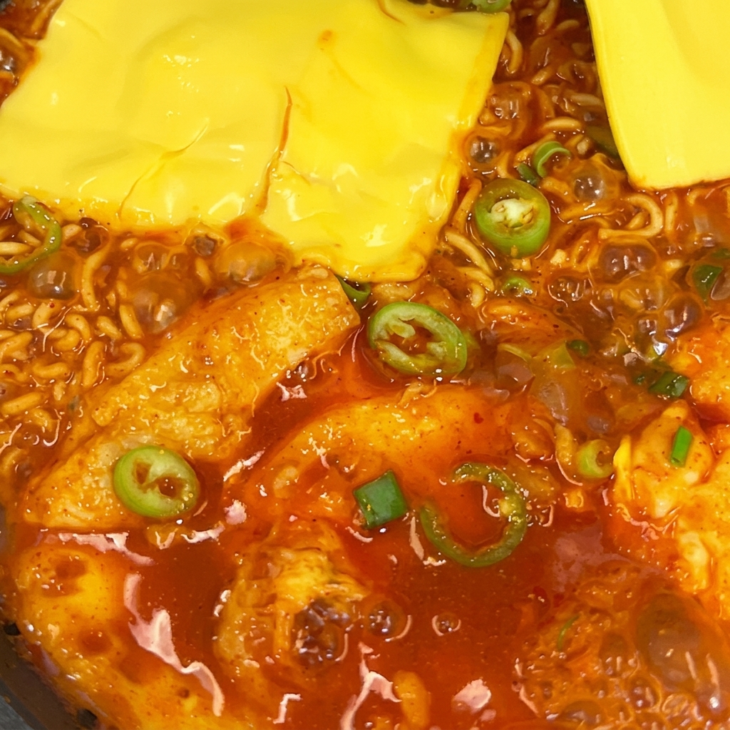Deux tranches de fromage jaune fondant sur des nouilles ramen épicées dans une poêle.