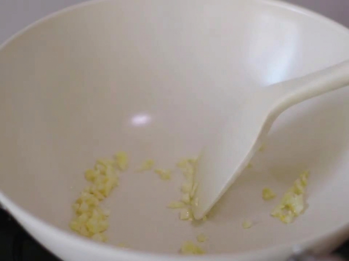 Champignons shiitake hachés et ail émincé en train de revenir dans une poêle blanche avec une spatule.