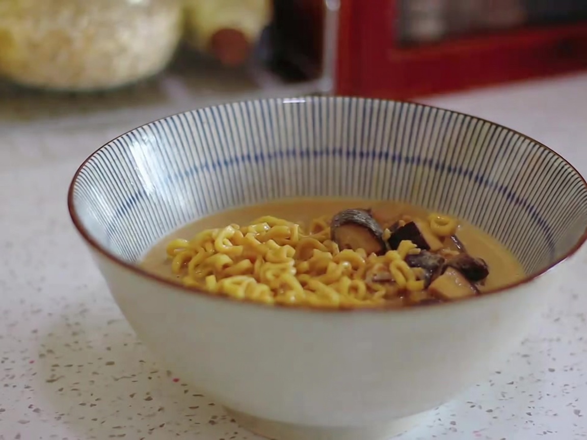 Nouilles ramen et bouillon crémeux versés à la louche dans un bol à rayures.