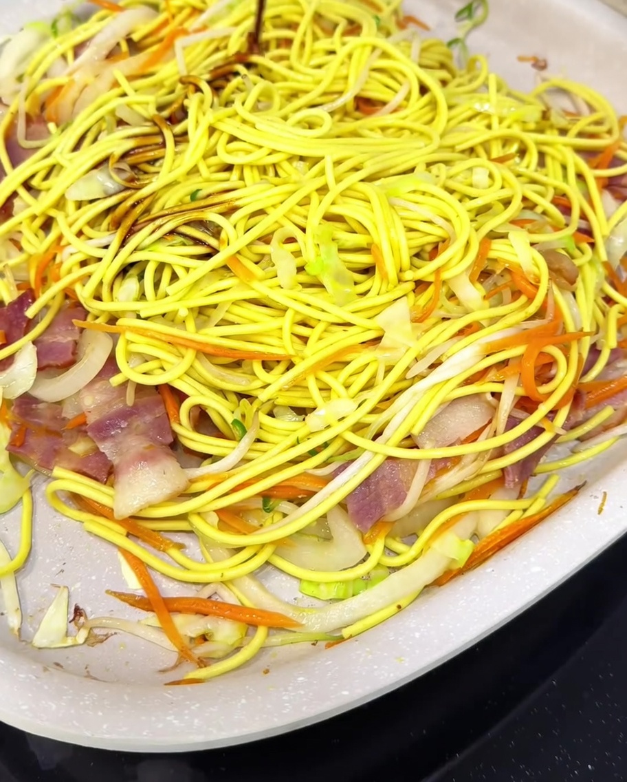 Nouilles et légumes mélangés à la sauce dans la poêle.