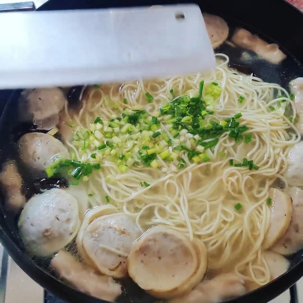 Vue de dessus dune casserole contenant des nouilles et des boulettes, garnie doignons verts hachés.