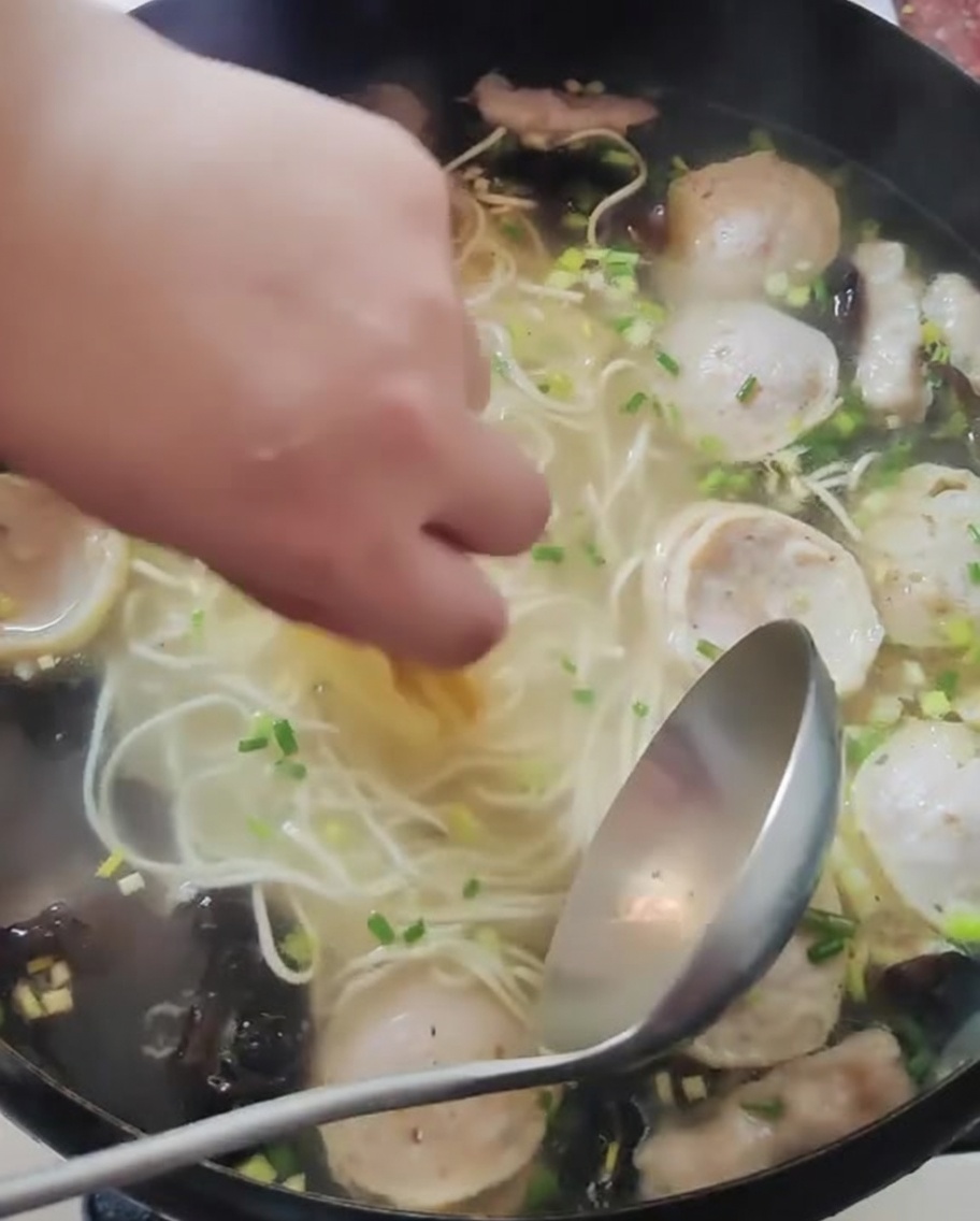Main plaçant de fines tranches de citron jaune dans une casserole de nouilles et de bouillon.