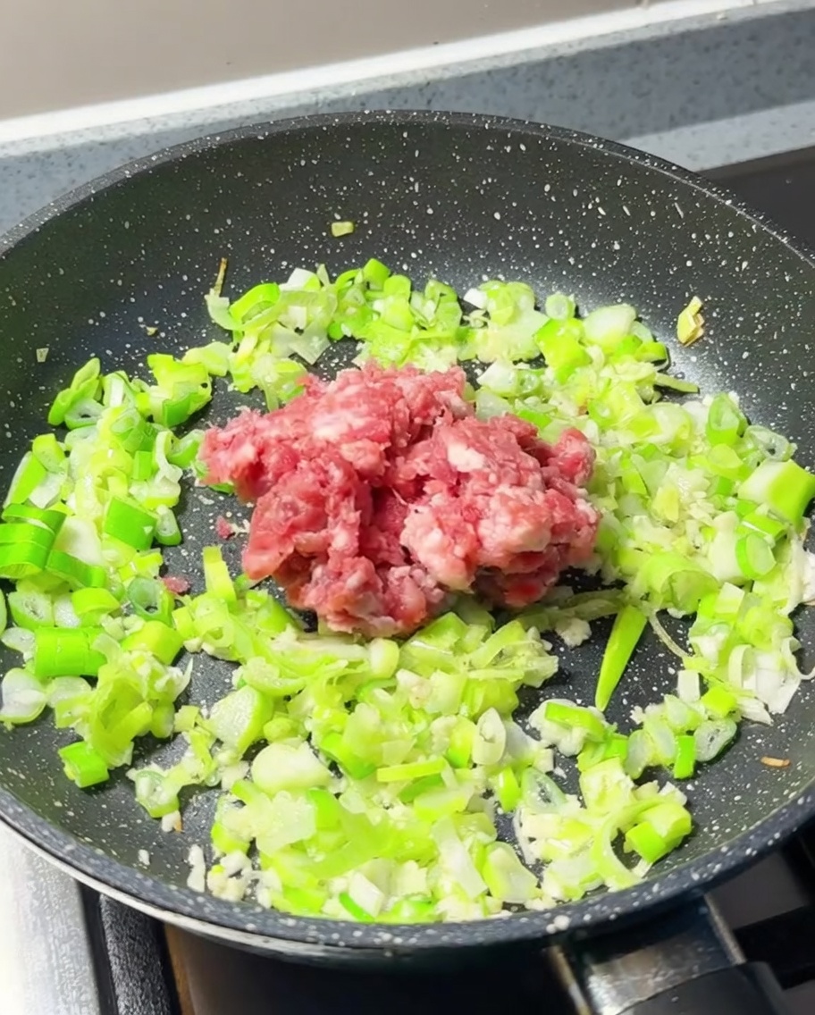 Viande hachée fraîche déposée au centre de la poêle avec les aromates.