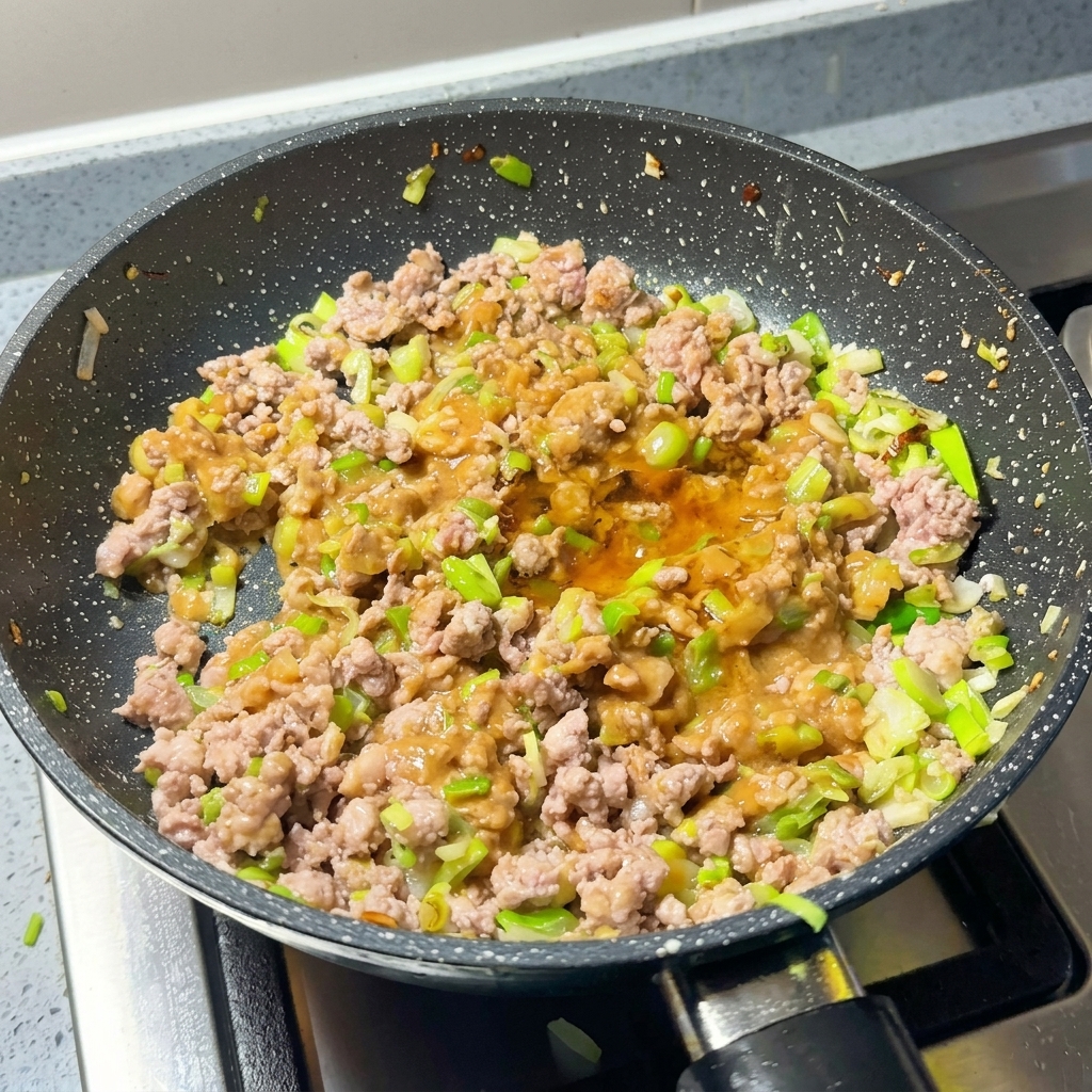 Mélange de viande et miso dans la poêle avec ajout de piment et de sucre.