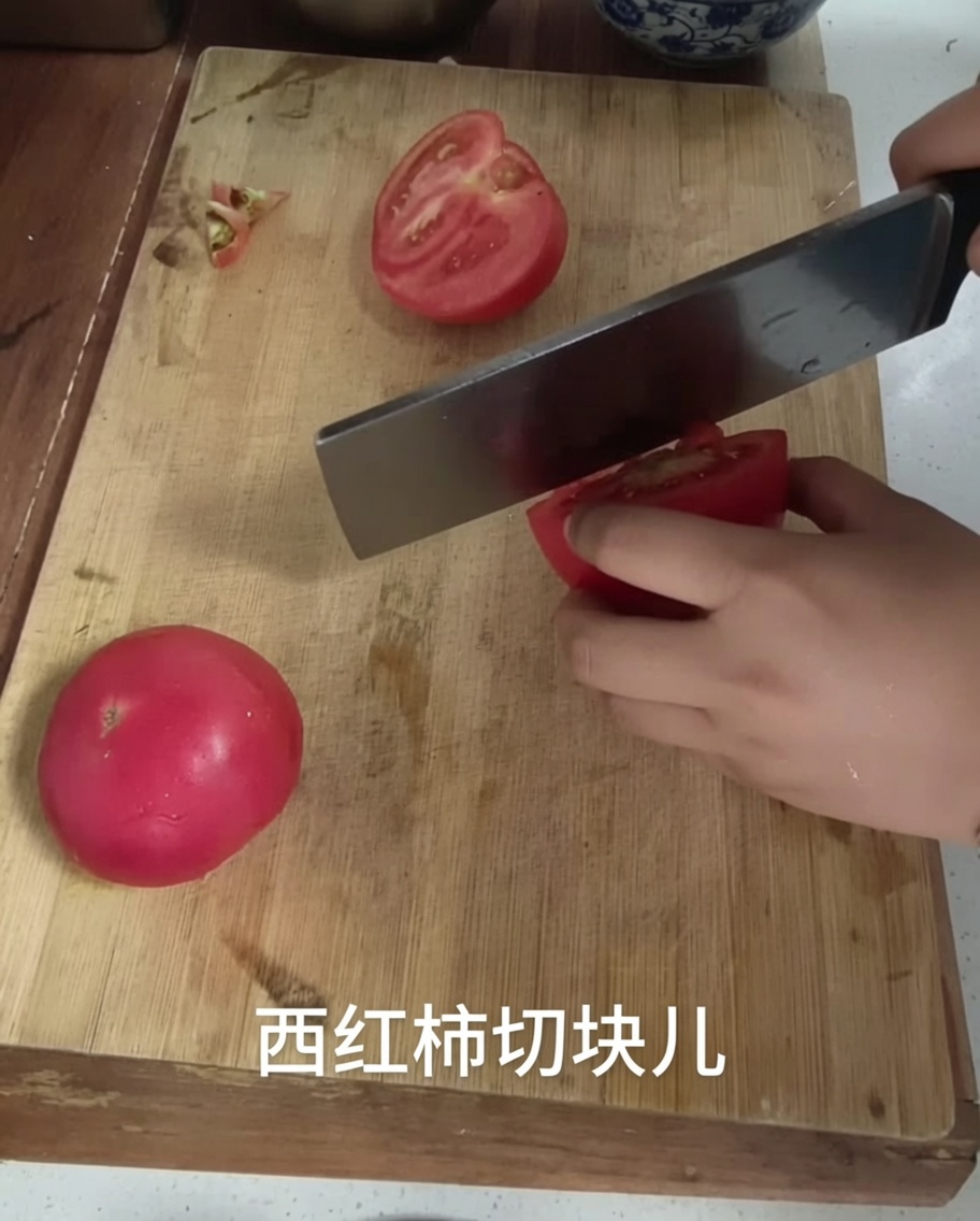 Un couteau de cuisine coupant une tomate en morceaux sur une planche à découper.