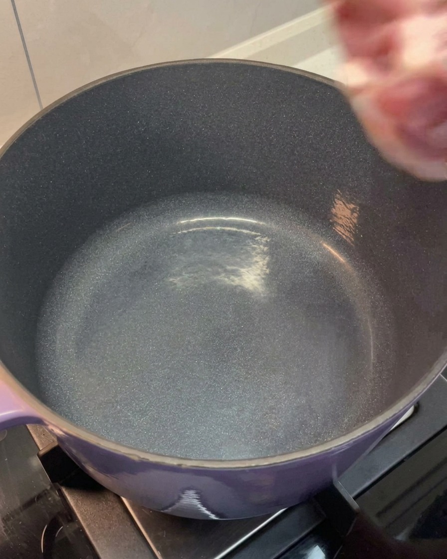 La poitrine et los de porc rincés étant placés dans une grande marmite violette.