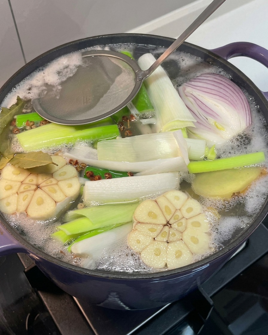 Une passoire en métal retirant la mousse grise à la surface du bouillon en ébullition.