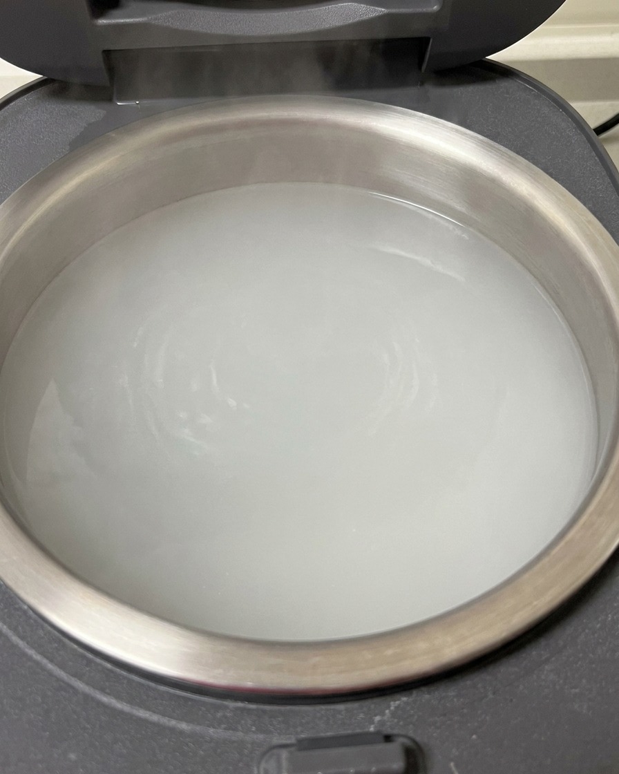 Gros plan sur des travers de porc crus immergés dans le pot dun cuiseur à riz rempli deau bouillante.