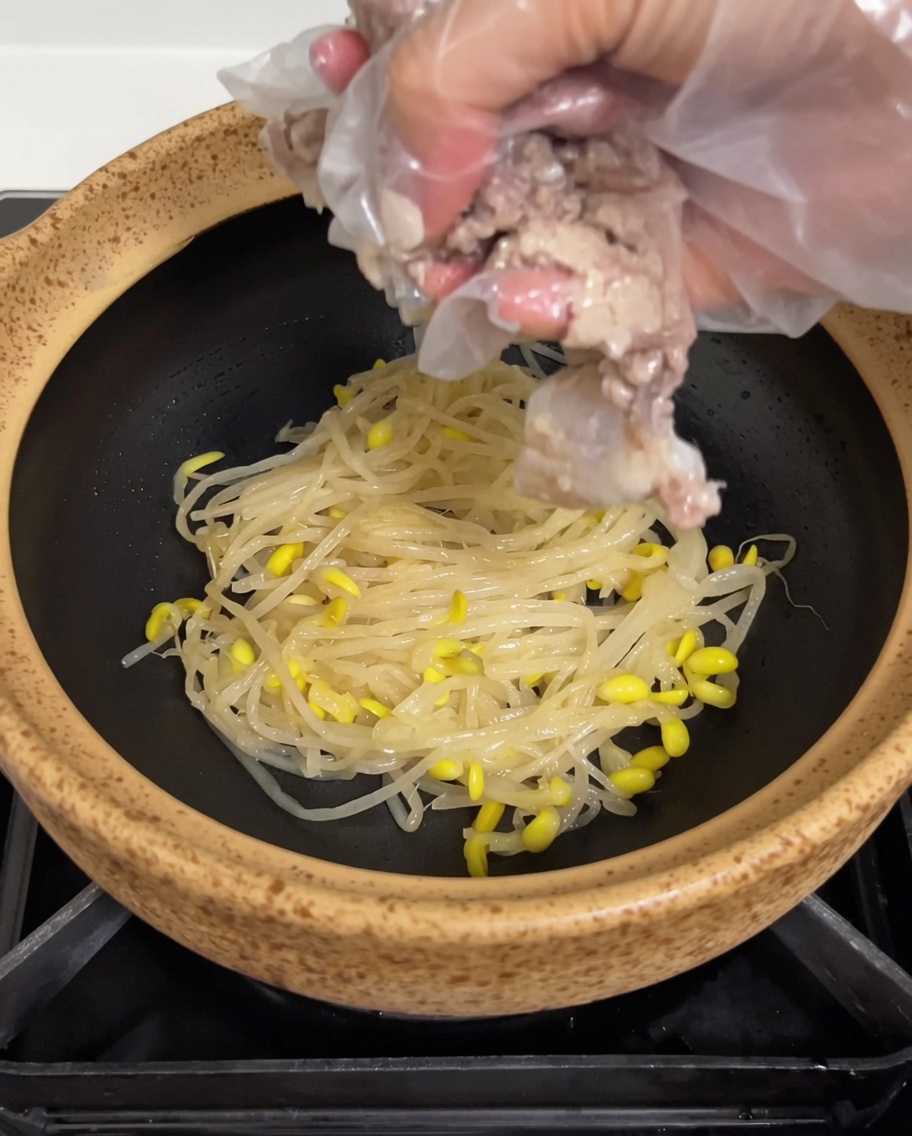 Des travers de porc cuits déposés sur le lit de pousses de soja dans le pot en terre cuite.