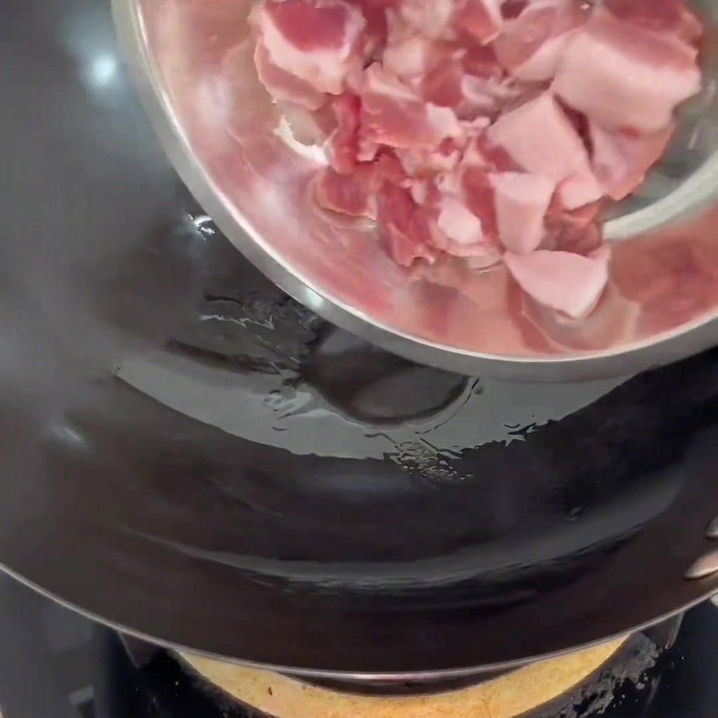 Tranches de porc déposées dans un wok chaud avec un peu dhuile.