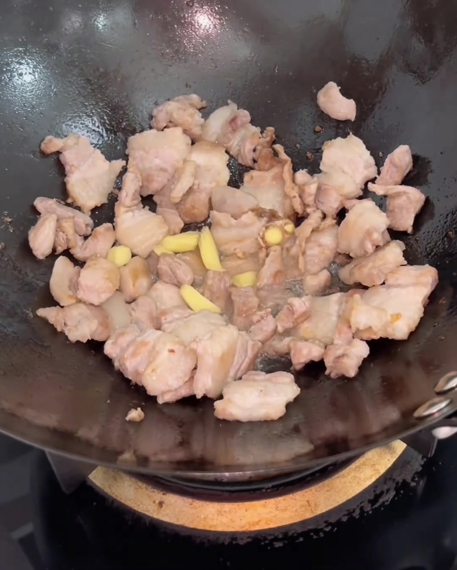 Tranches de gingembre ajoutées au porc dans le wok.