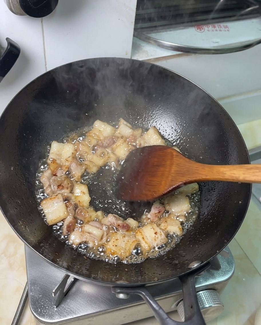 Morceaux de poitrine de porc en train de frire dans le gras fondu dans un wok.