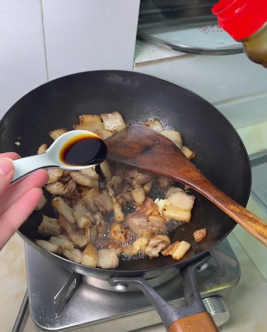 Sauce soja versée sur la poitrine de porc sautée dans un wok.