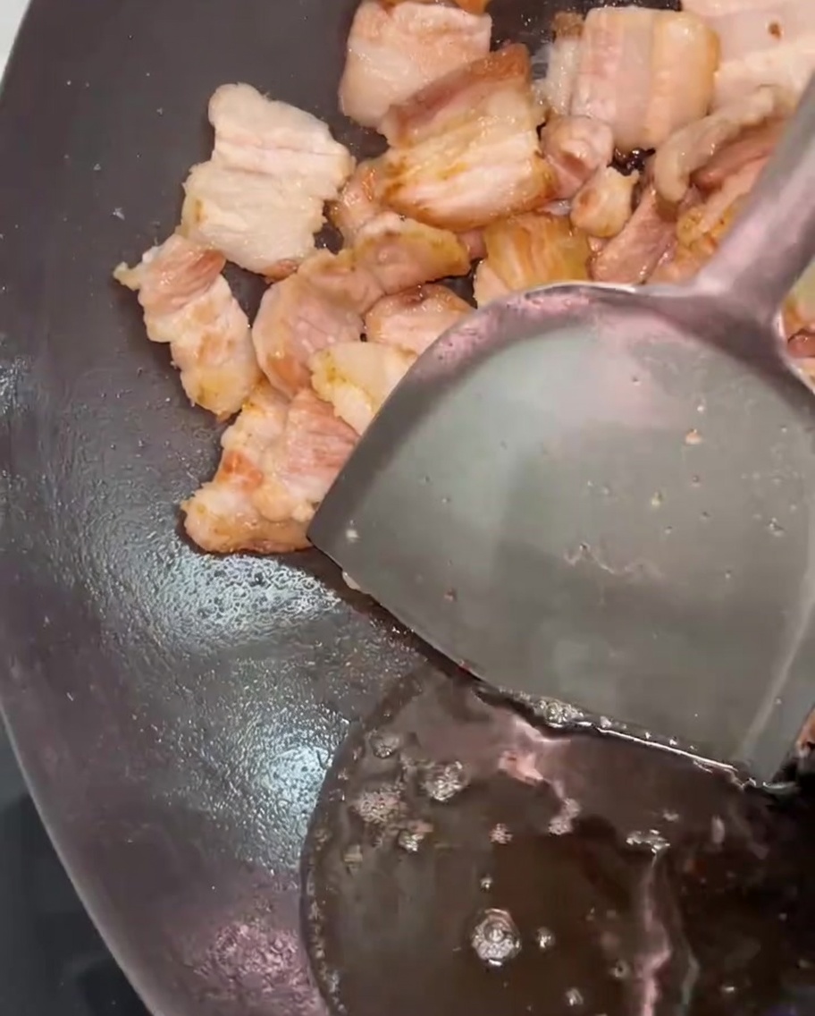 Une spatule métallique poussant le porc sur le côté pendant que le gras excédentaire est retiré du wok.