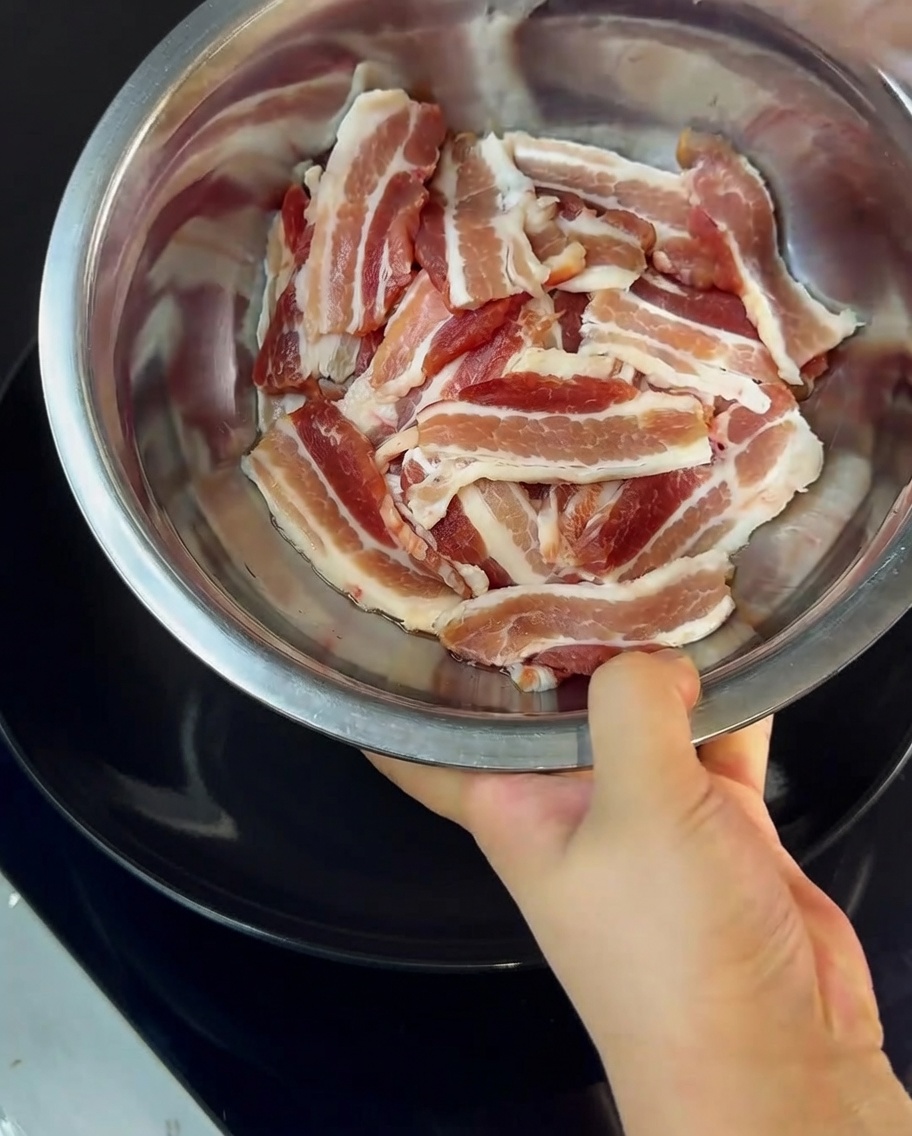 Gros plan sur des tranches de poitrine de porc mélangées à de la fécule de maïs dans un bol en métal.