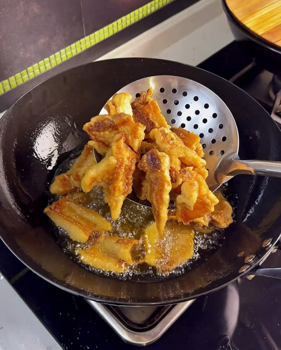 Poitrine de porc croustillante dorée retirée de lhuile avec une écumoire en inox.