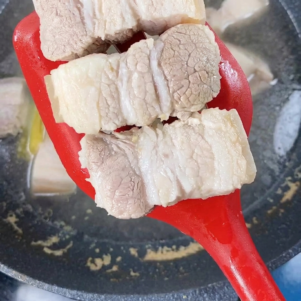 Morceaux de poitrine de porc blanchis retirés de leau bouillante avec une spatule rouge.