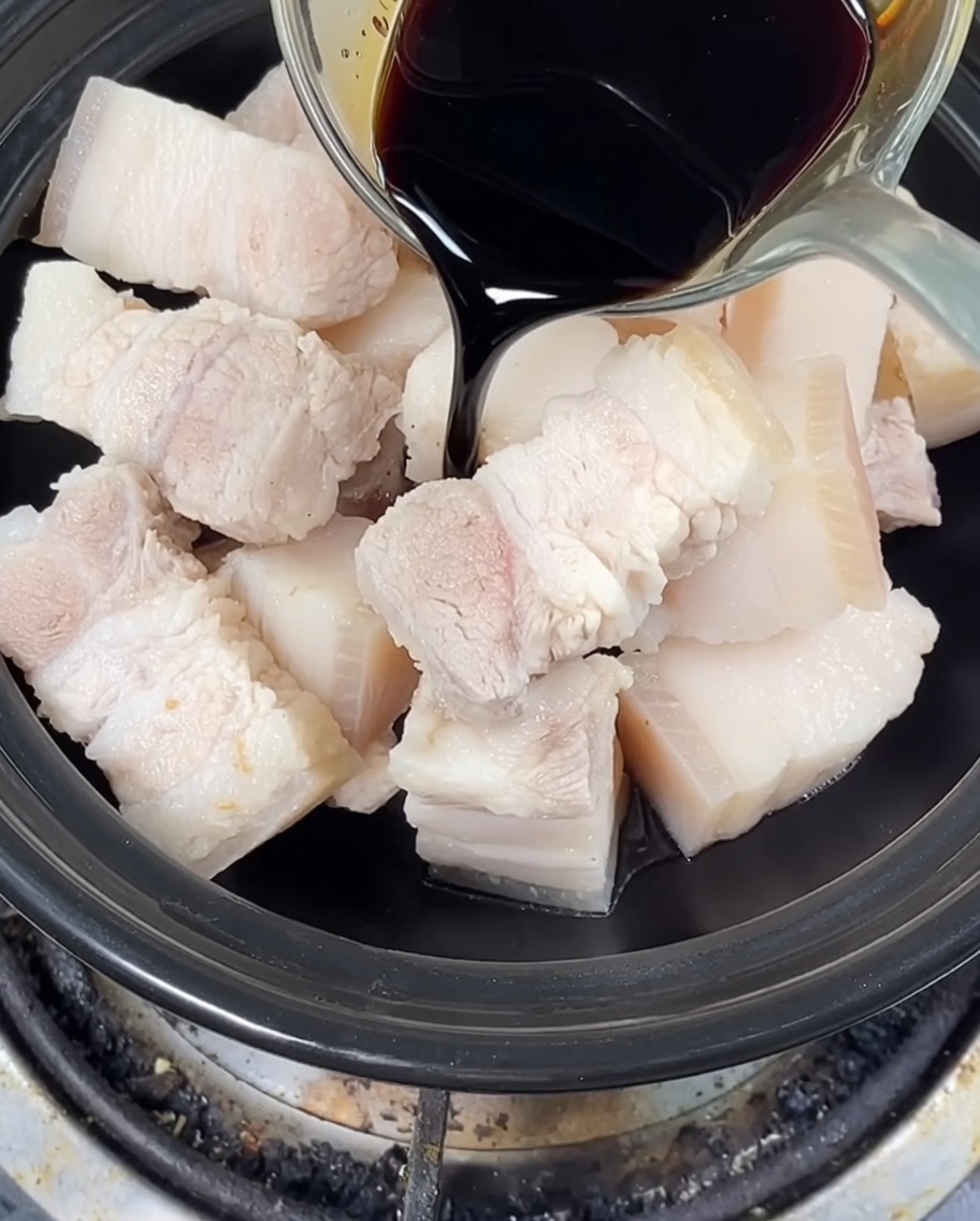 Sauce soja foncée et claire versées sur le porc dans la cocotte, avec le sucre candi ajouté.