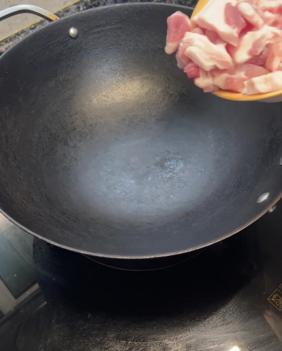 Tranches de poitrine de porc crue déposées dans un wok chaud et vide.