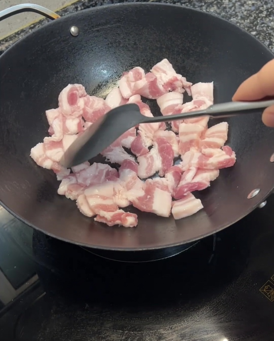 Tranches de poitrine de porc sautées dans un wok avec une spatule, montrant des signes de brunissement.