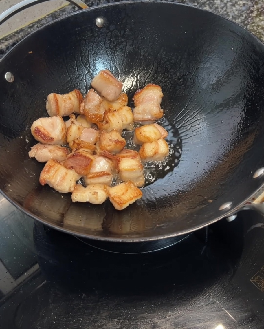 Gousses dail ajoutées dans le wok avec la poitrine de porc dorée.