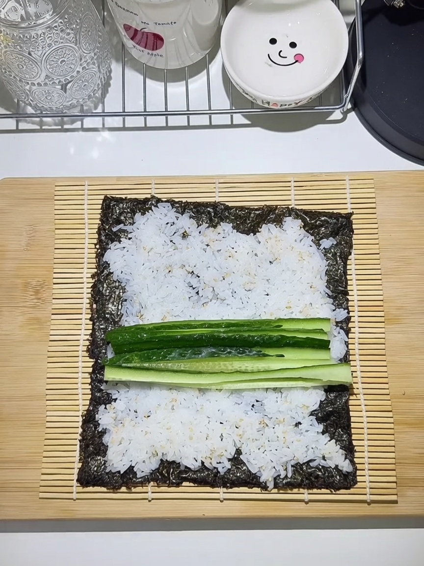 Tapis en bambou avec une feuille dalgue garnie de riz, concombre, carotte, œuf et bœuf.