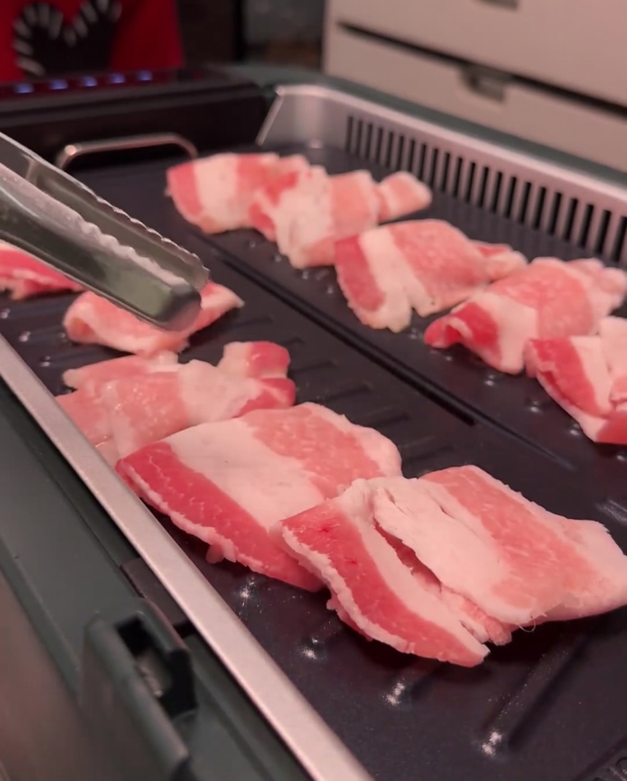Tranches de poitrine de porc qui dorent et cuisent sur la surface du gril.