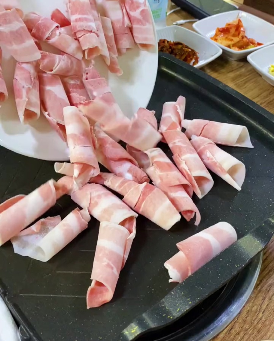 Fines tranches de poitrine de porc crue déposées sur une plaque chaude.