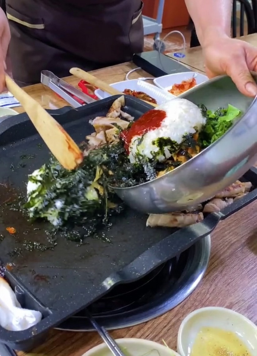 Riz, légumes et algues versés depuis un bol en métal sur une plaque avec du porc.