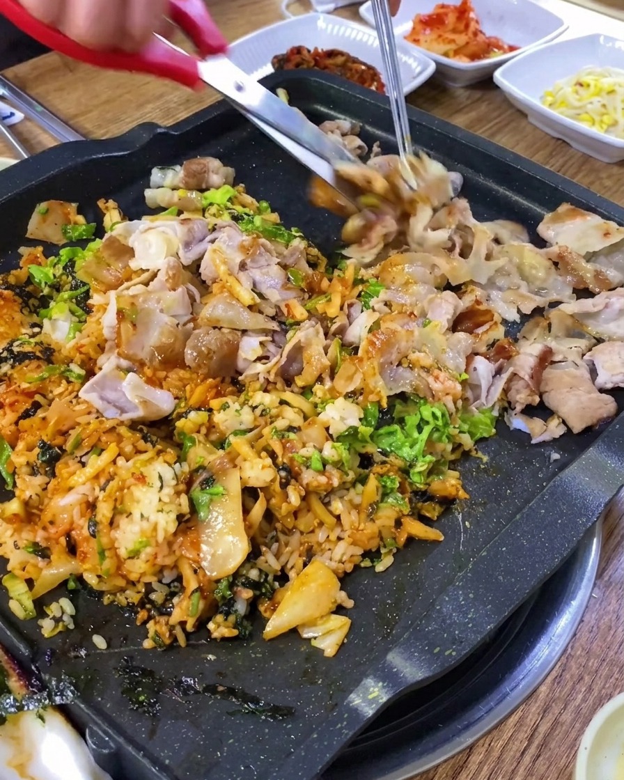 Ciseaux de cuisine coupant le porc grillé en petits morceaux sur une plaque.