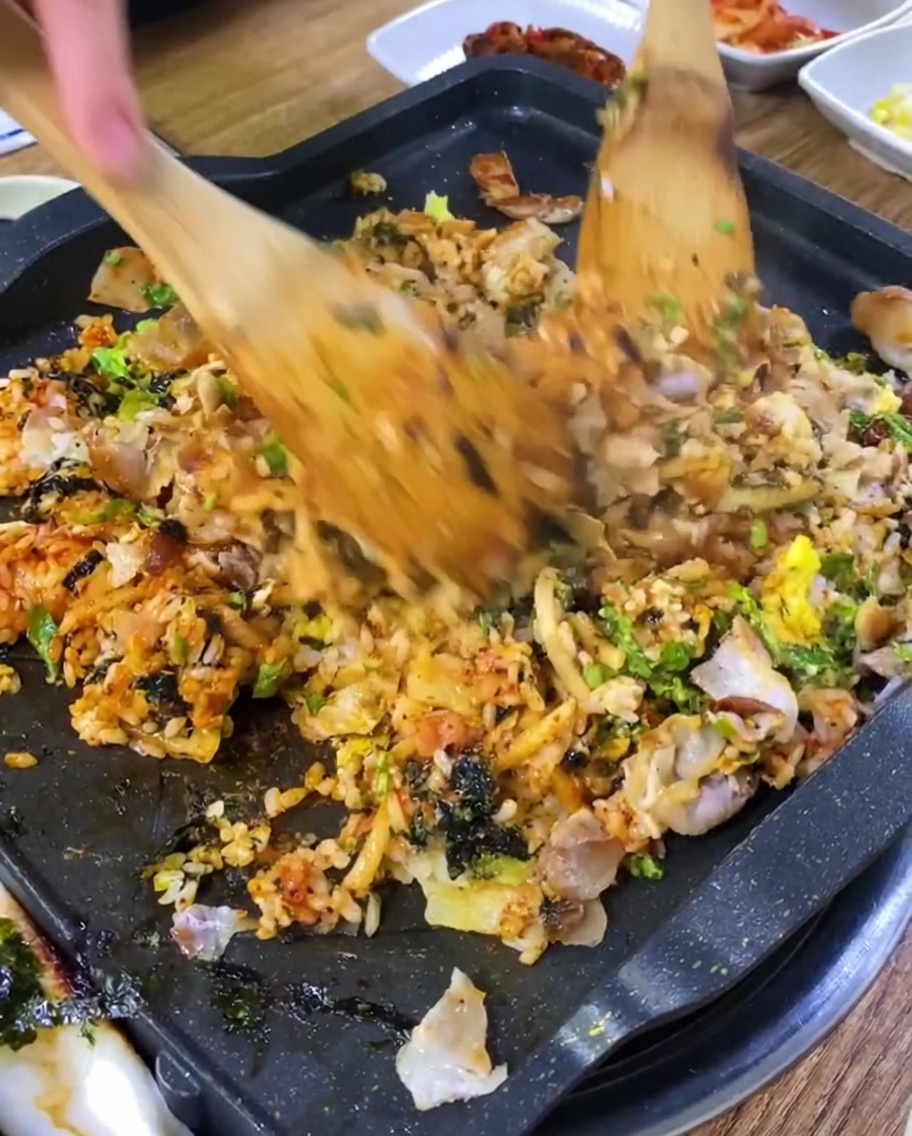 Riz frit en cours de cuisson avec des morceaux de porc sur une plaque chaude.