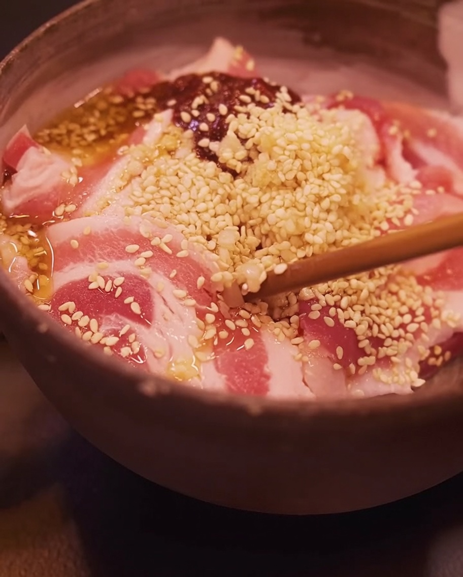 Gros plan avec des baguettes mélangeant la poitrine de porc marinée dans un bol.