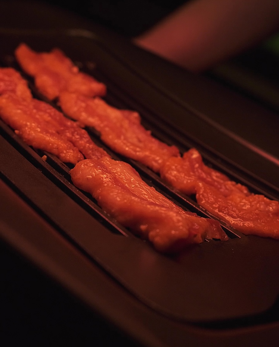 Tranches de poitrine de porc marinée grésillant sur une surface de gril électrique chaude.