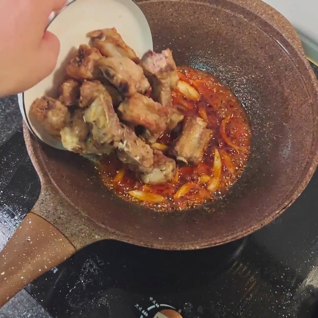 Travers de porc frits mélangés avec la sauce épicée et les aromates dans une poêle.